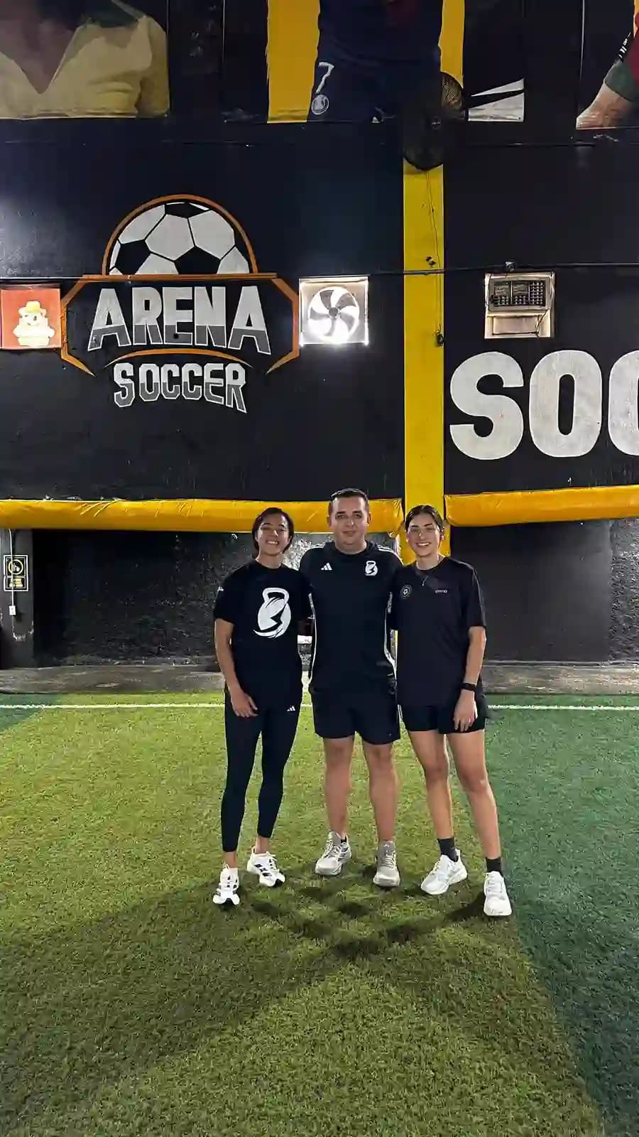 Coach Yair Garza con dos jugadoras frente al logo de Arena Soccer